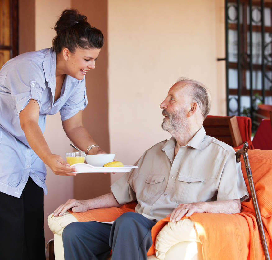 aide à domicile qui sert un repas à un homme senior